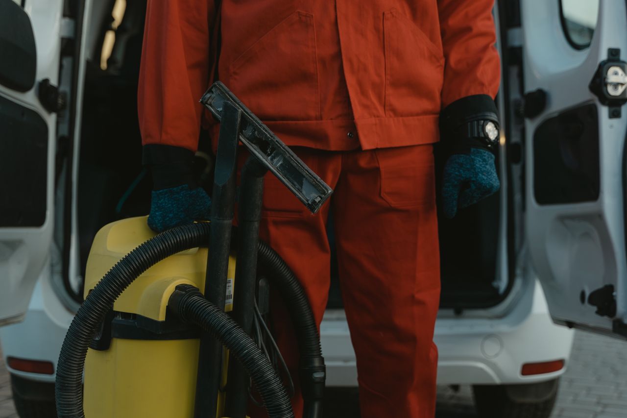services-01 A professional cleaner in a red uniform holding a vacuum near a van, ready for service.